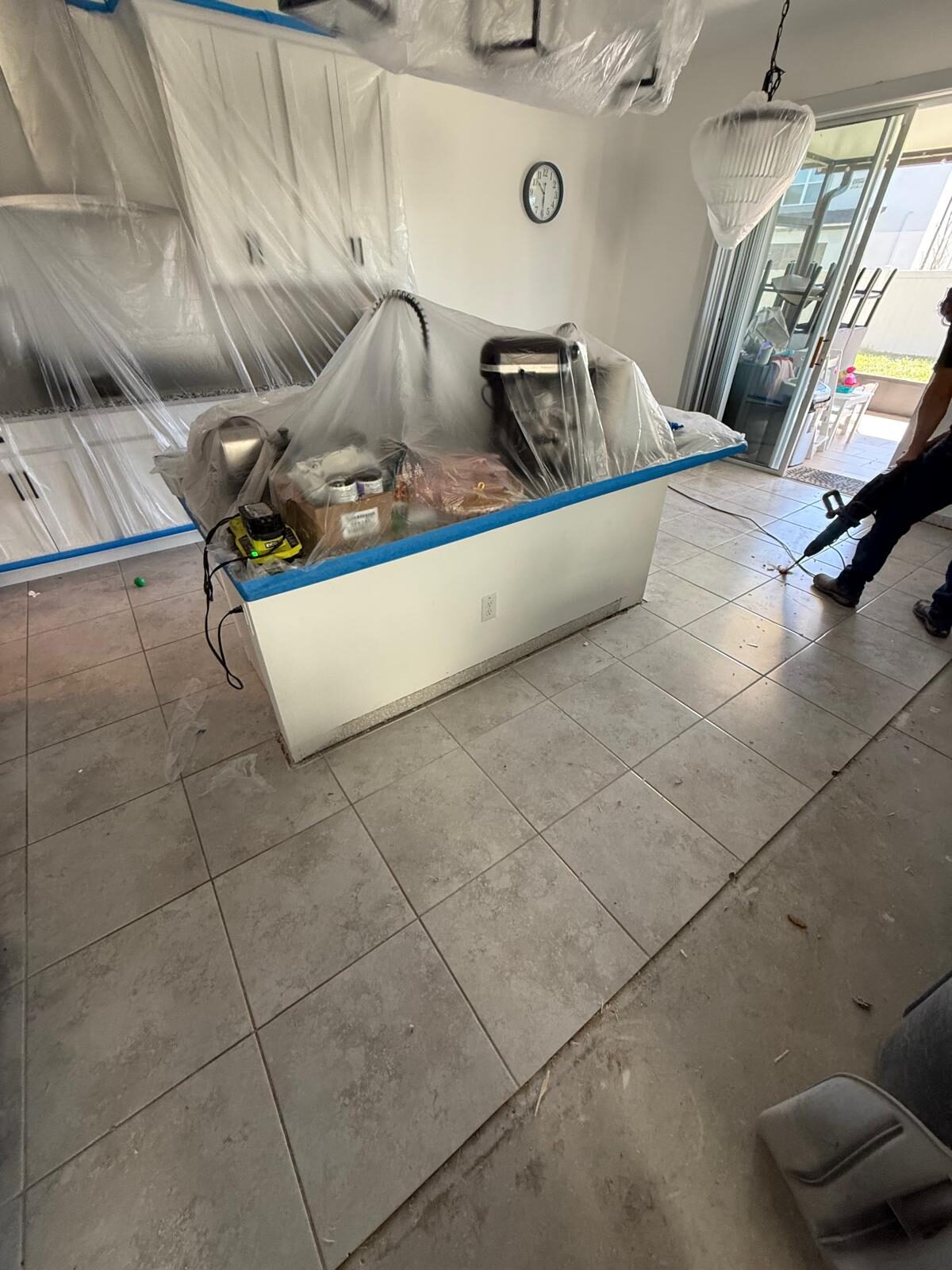 Kitchen with covered cabinets, tile flooring, and worker preparing the floor