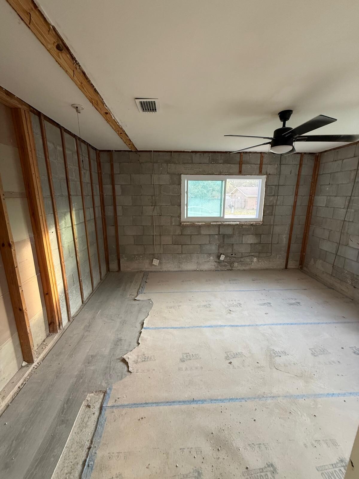 Demolished interior room with exposed cinder block, new window, and ceiling fan