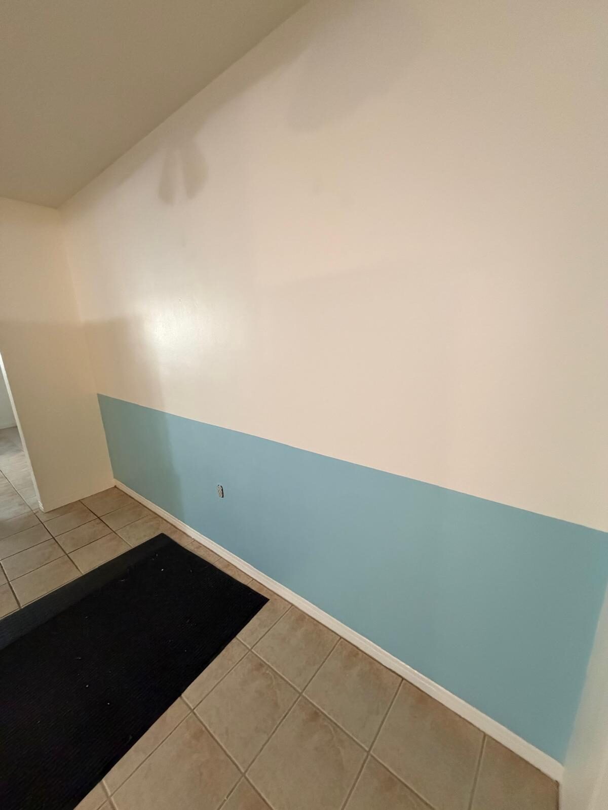 Interior wall partially painted light blue with clean tile floor and black mat