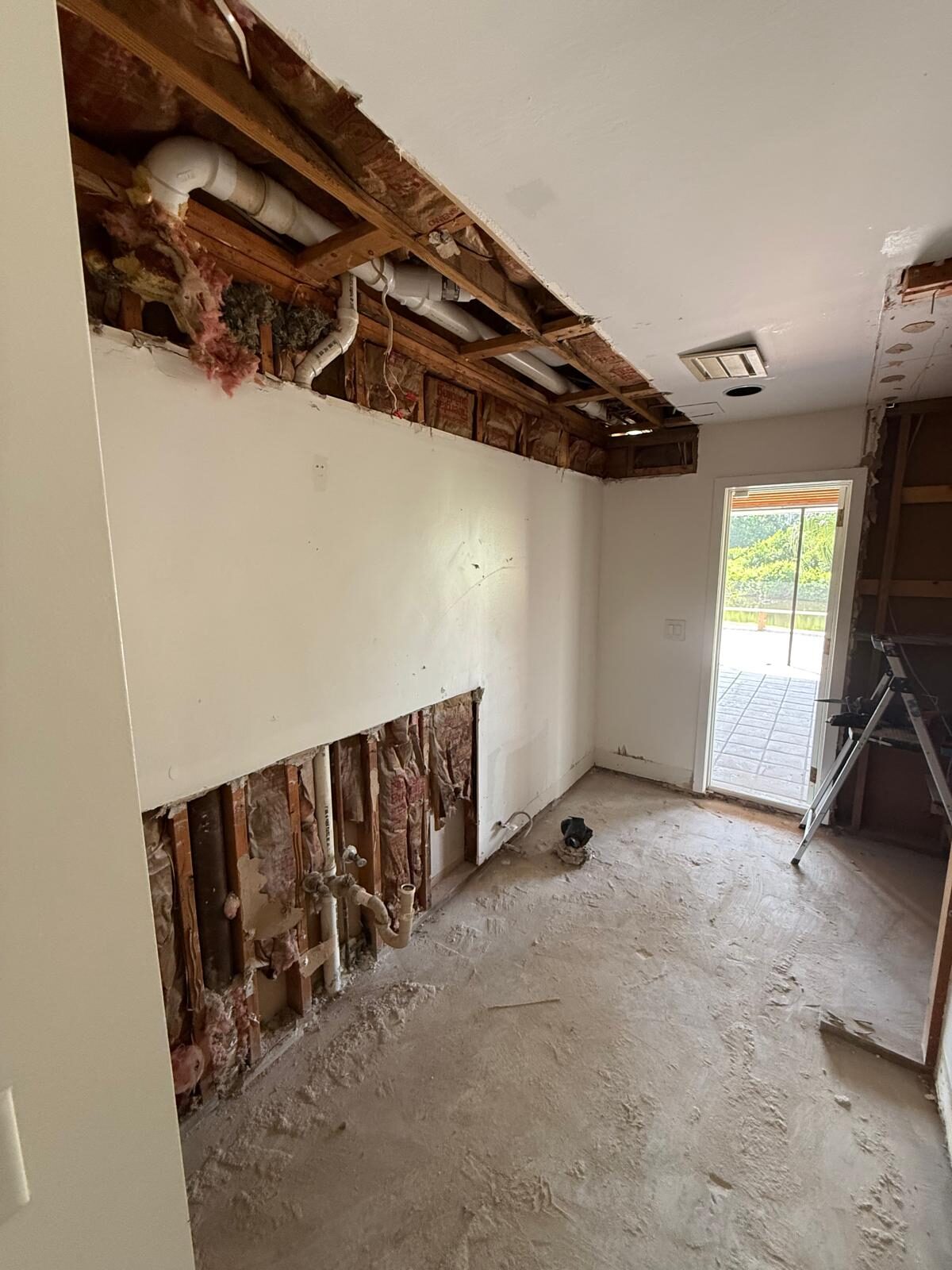 Kitchen renovation with ceiling removed revealing pipes and insulation, a door leads to outside