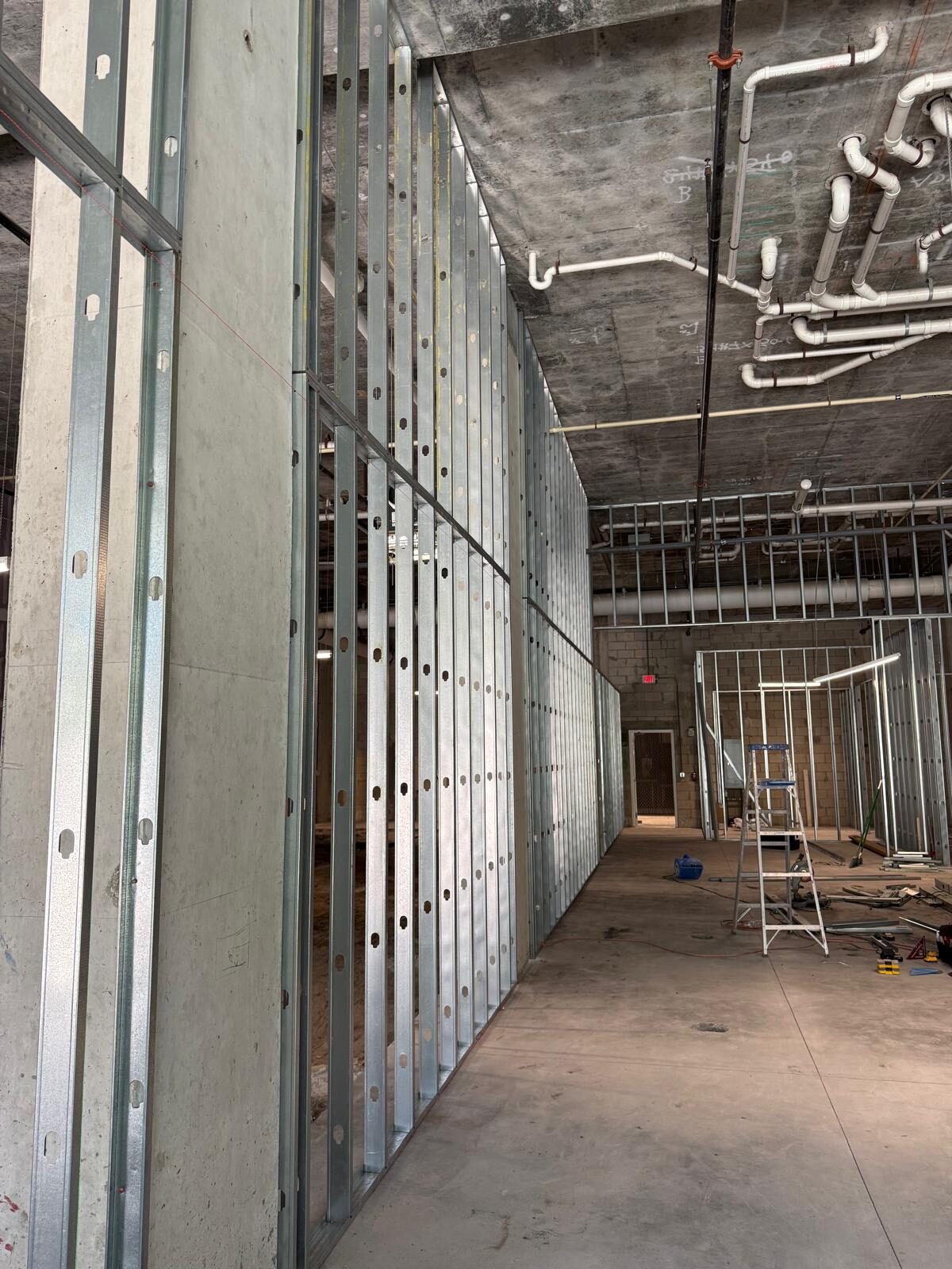 Long hallway in commercial building with metal stud framing and exposed pipes