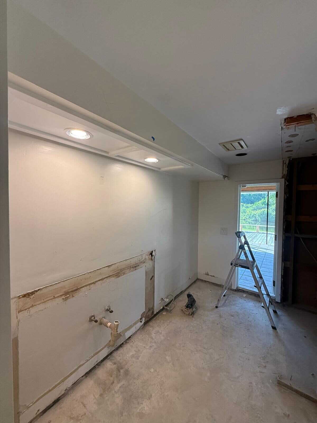 Kitchen renovation showing exposed wall, removed sink, and a ladder by the door