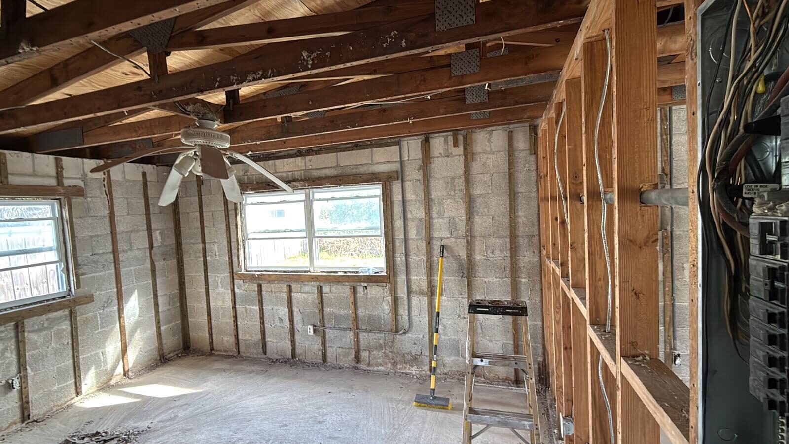 Residential interior stripped to studs and block walls, with a ceiling fan