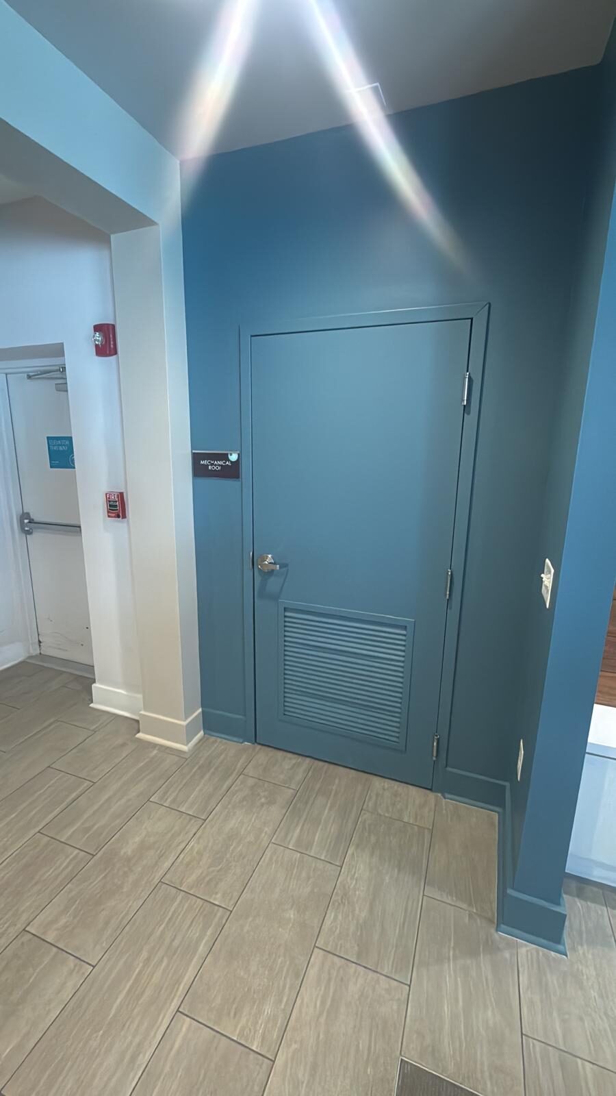 Newly painted blue commercial hallway with a matching access door and tiled floor
