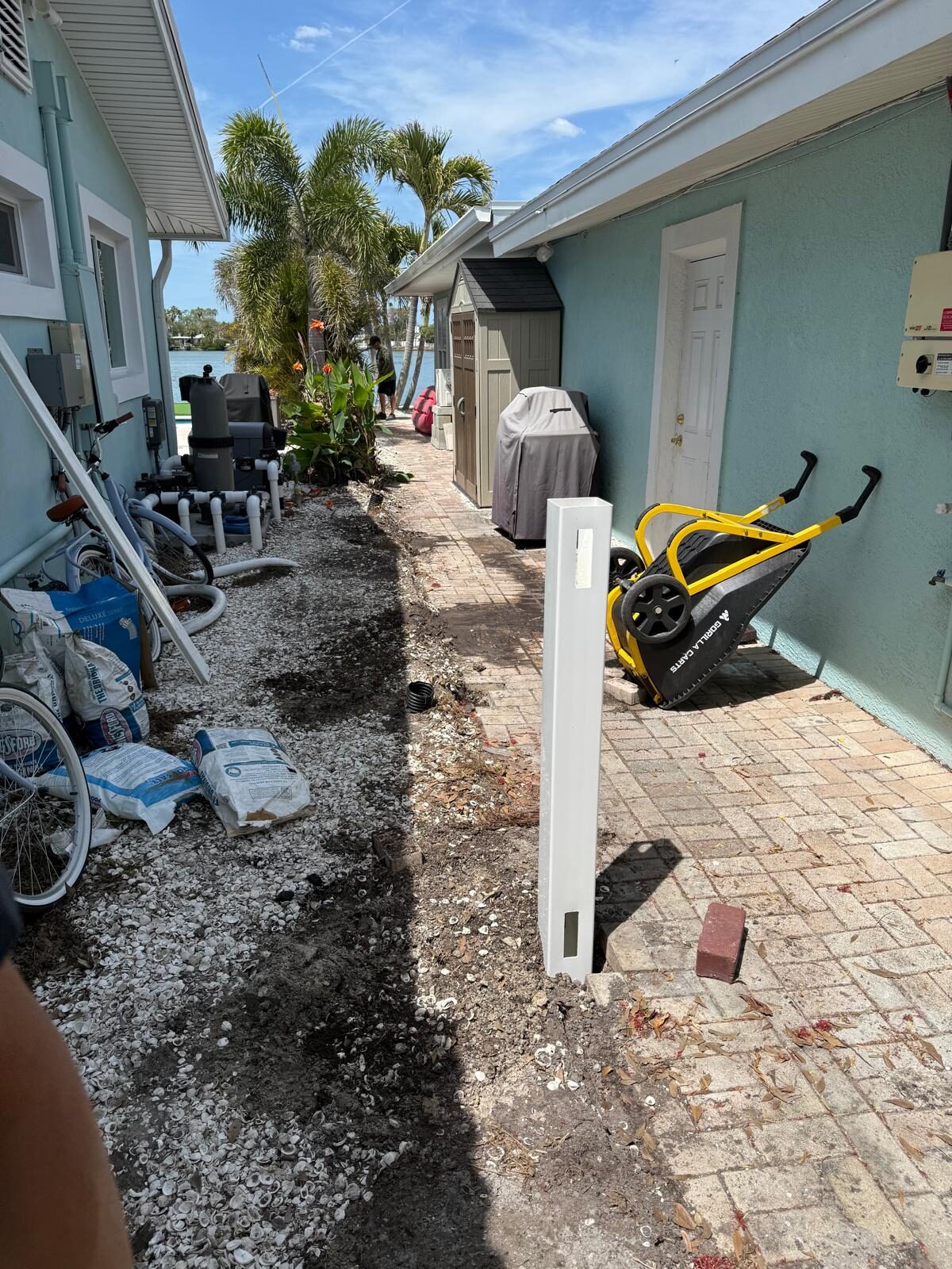 Narrow exterior space between two buildings, showing existing pavers and cleared ground