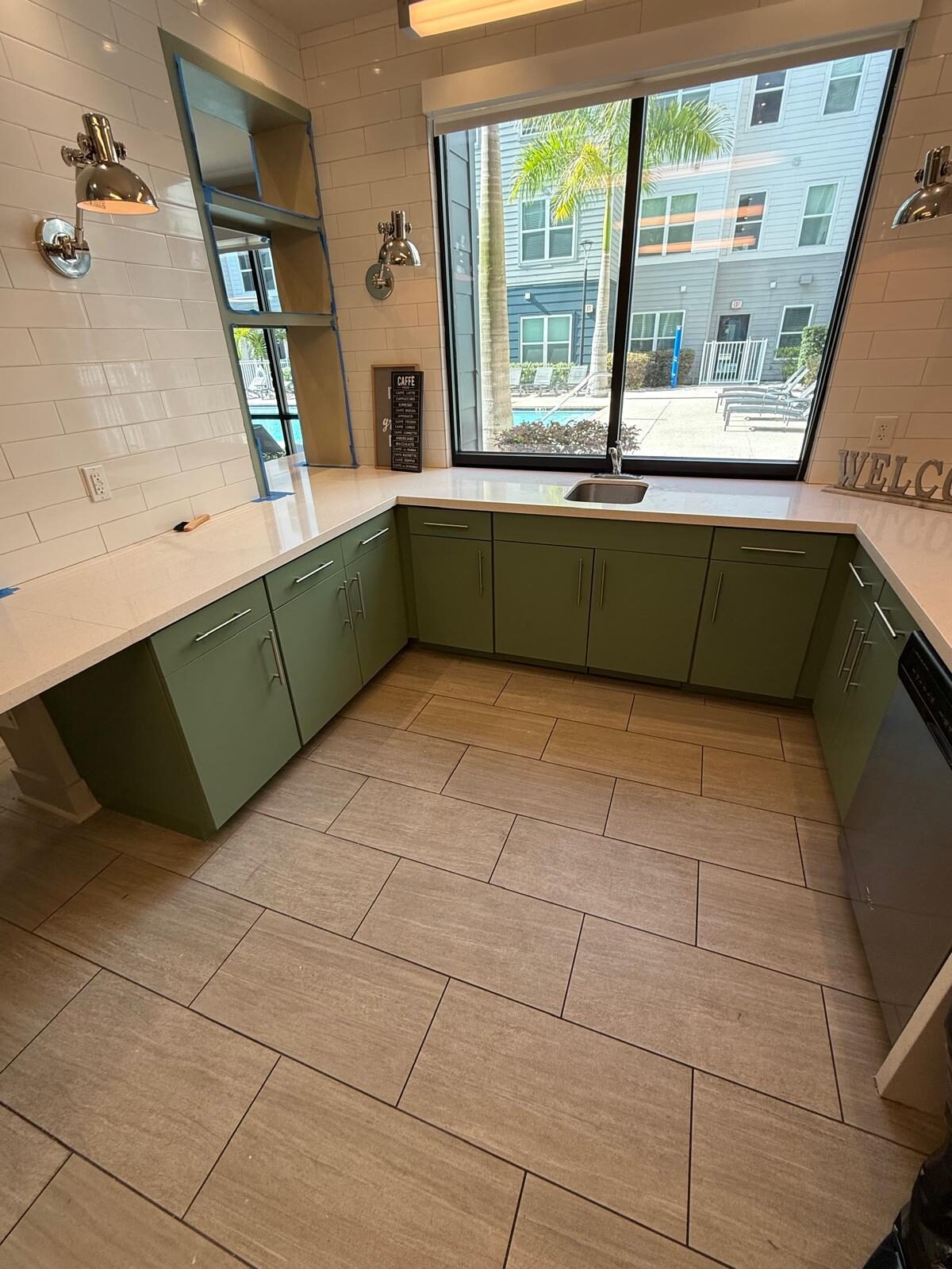 Spacious commercial kitchen with green base cabinets, light countertops, and large windows