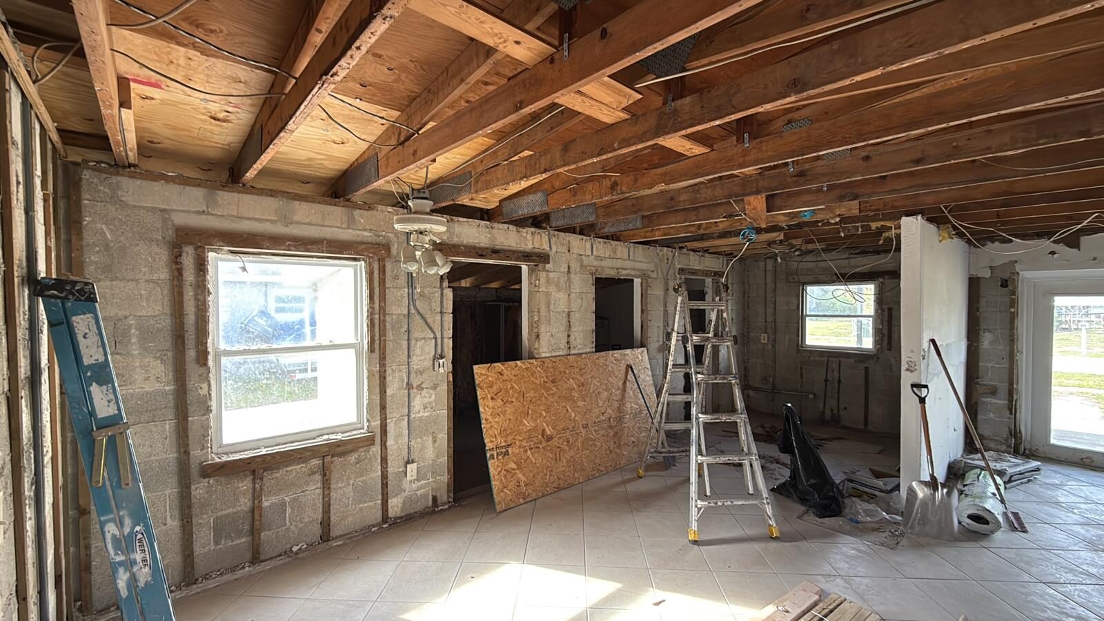 Interior room during demolition, showing exposed block walls, studs, and ceiling joists