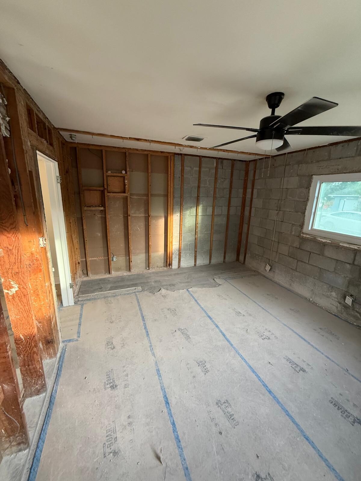 Interior room during renovation, walls stripped to studs, with exposed block and new window