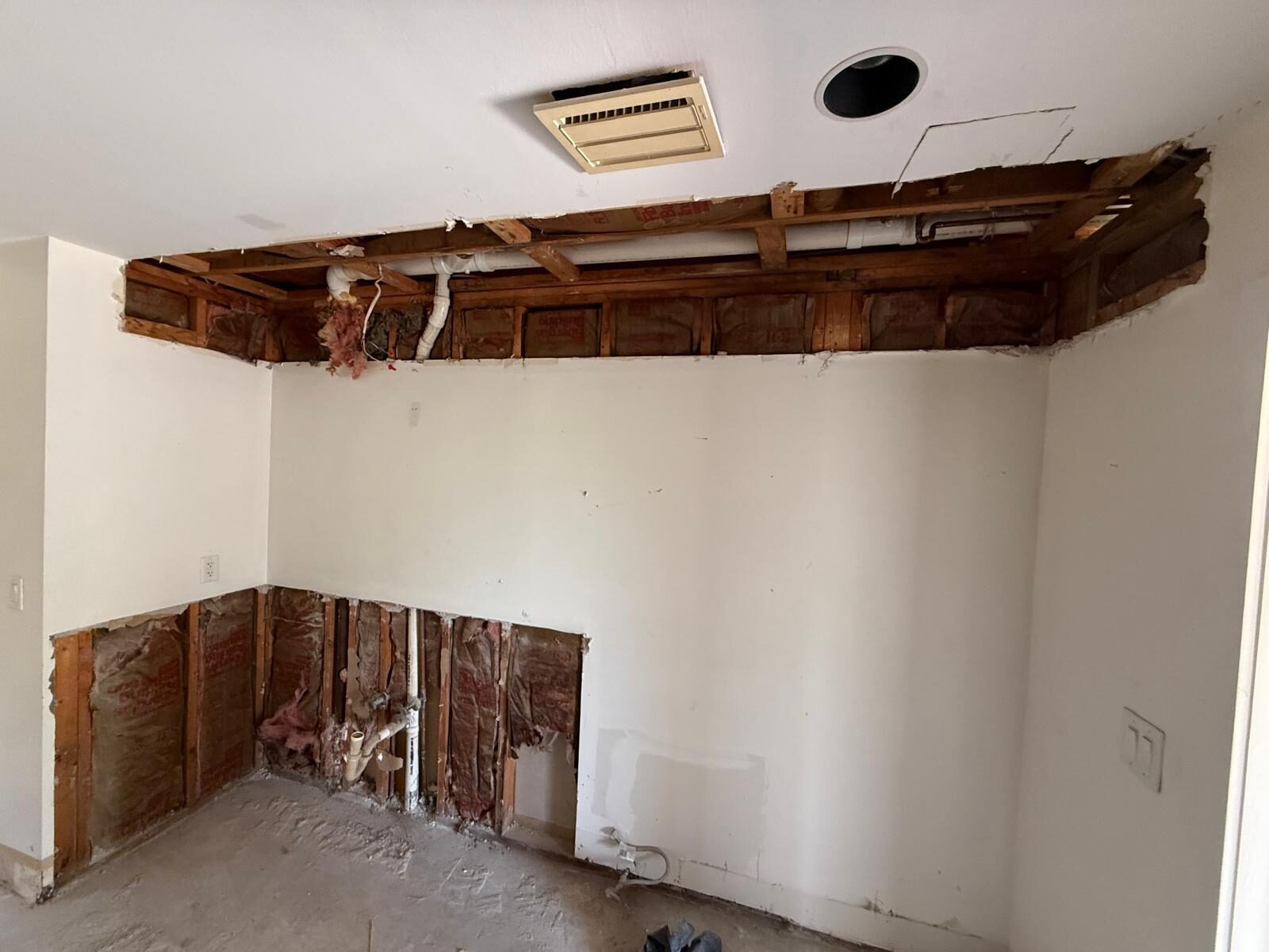 Kitchen area under renovation with ceiling and wall panels removed, exposing framing