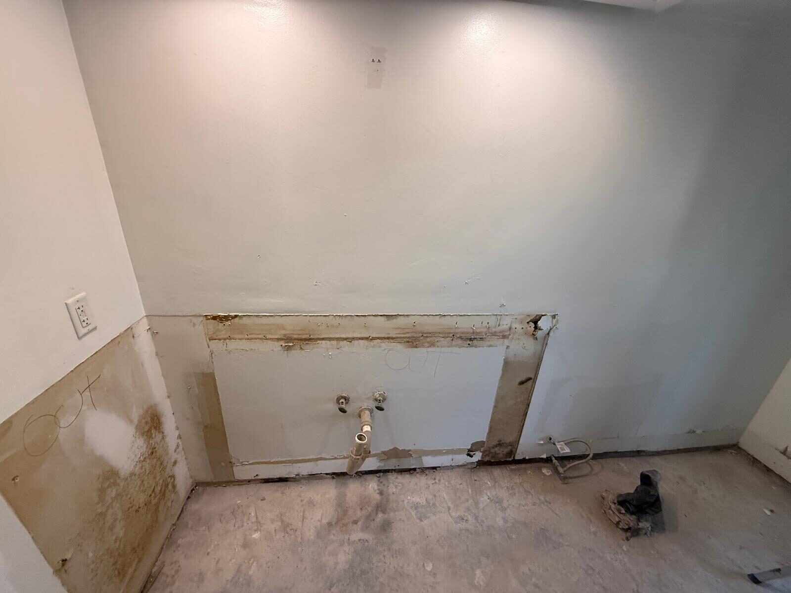 Demolished kitchen area with drywall removed, exposing plumbing connections