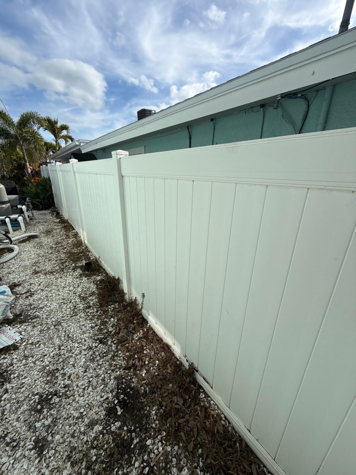 Newly installed white vinyl privacy fence alongside a residential property with a blue house