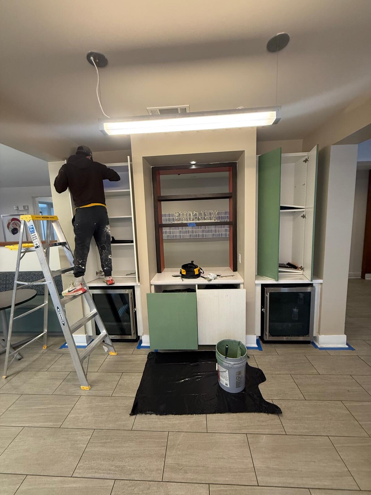 Worker on a ladder painting built-in cabinets in a kitchen or living area