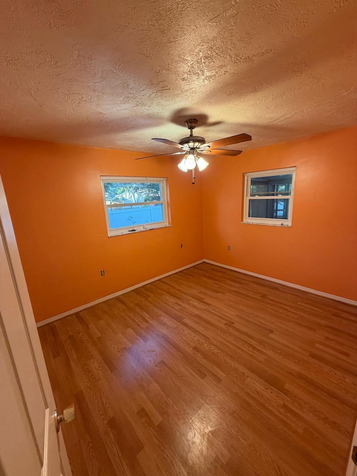 Bright orange bedroom with a ceiling fan, two windows, and hardwood flooring