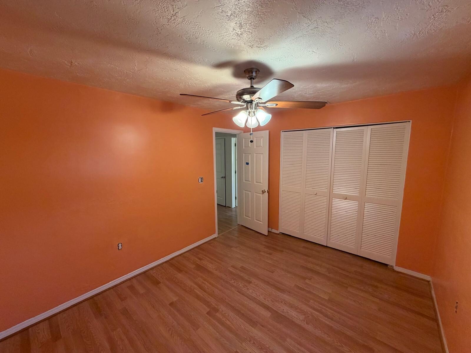 Bedroom with vibrant orange walls, a ceiling fan, and hardwood floors